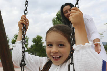 Happy mother with daughter using swing in park - SYEF00489