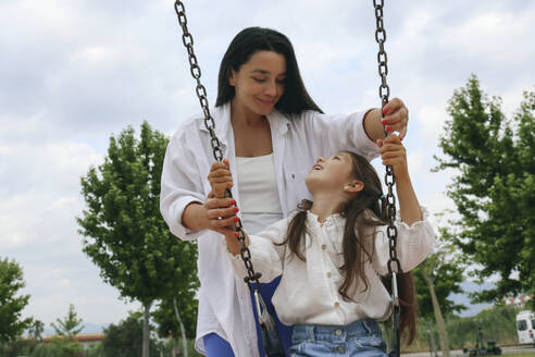 Lächelnde Mutter mit Tochter, die auf einer Schaukel schaukelt - SYEF00491