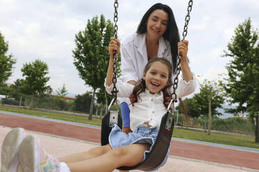 Happy mother with daughter swinging on swing - SYEF00492