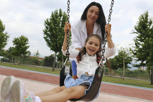 Glückliche Mutter mit Tochter, die auf einer Schaukel schaukelt - SYEF00492