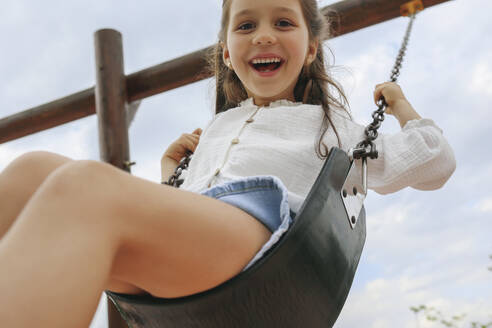 Happy girl swinging on swing under sky - SYEF00495
