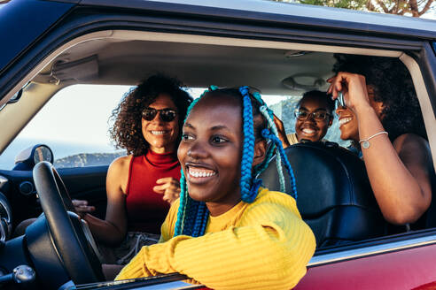 Happy multiracial women smiling happily while riding in modern automobile enjoying summer vacation during road trip having fun together - ADSF45229