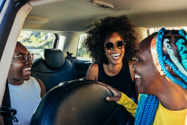 Cheerful multiracial friends smiling while sitting in automobile parked near sea having fun during summer trip - ADSF45231