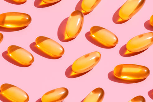 Composition of orange vitamin pills scattered on pink background in light studio - ADSF45245