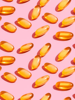 Top view composition of orange vitamin pills scattered on pink background in light studio - ADSF45246