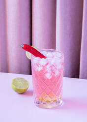 Clear glass filled with refreshing cold cocktail served with pepper and ice cubes placed on the table with lime - ADSF45260