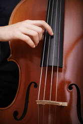 Closeup with crop anonymous female musician practicing music on acoustic cello by pulling strings with hand - ADSF45315