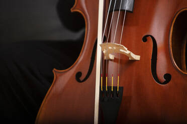 Closeup of wooden classic cello with metal strings and brown polished wooden part with bow placed on dark background in studio - ADSF45317