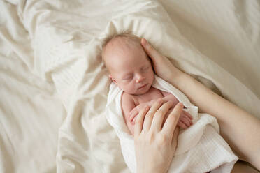 From above of crop mom caressing adorable little baby lying on white bed and sleeping in morning - ADSF45372