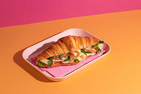 From above of delicious croissant with ham, cheese and rocket leaves placed on plate in colorful background - ADSF45390