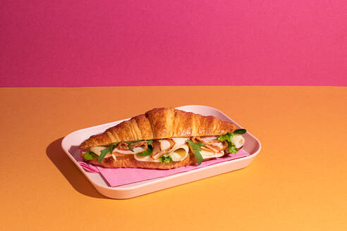 From above of delicious croissant with ham, cheese and rocket leaves placed on plate in colorful background - ADSF45392