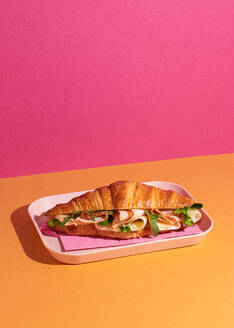 From above of delicious croissant with ham, cheese and rocket leaves placed on plate in colorful background - ADSF45395