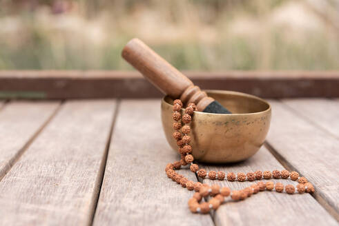 Golden metal singing bowl with beads placed on wooden surface on sunny day - ADSF45403