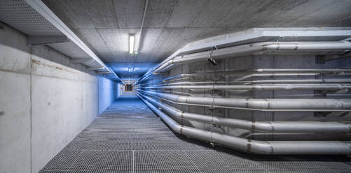 Empty underground corridor with drainage system and metal pipelines for transporting water and gas with electricity lines on ceiling - ADSF45411