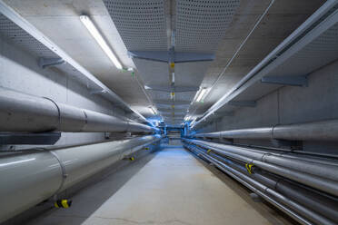Empty underground corridor with drainage system and metal pipelines for transporting water and gas with electricity lines on ceiling - ADSF45415