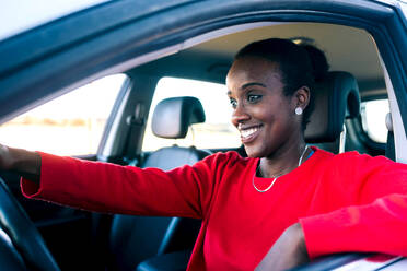 Positive female driver in casual wear steering wheel of automobile and smiling while looking forward and sitting on driver seat - ADSF45450