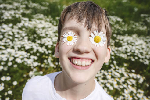 Happy boy with chamomile flowers over eyes - EYAF02696