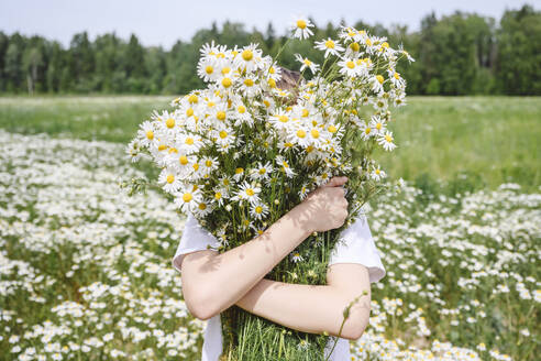 Boy holding bunch of chamomile flowers over face - EYAF02697