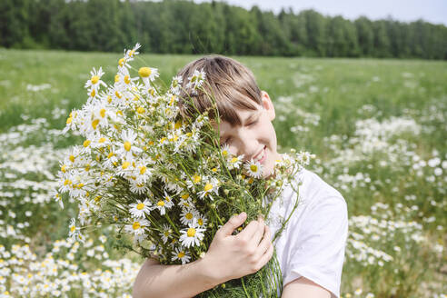 Smiling boy with closed eyes holding chamomile flowers - EYAF02698