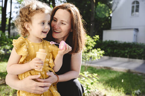 Smiling mother looking at daughter holding bubble wand - EYAF02707