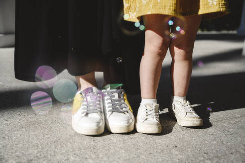 Mother and daughter standing on floor wearing shoes at sunny day - EYAF02708