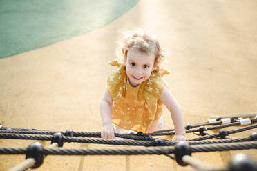Lächelndes Mädchen klettert am Seil im Klettergerüst - EYAF02719