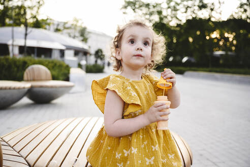 Contemplative girl in yellow dress holding bubble wand - EYAF02720