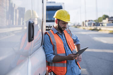 Logistics worker using tablet PC standing by truck - UUF29563