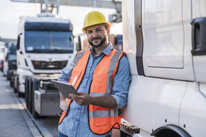 Happy truck driver leaning on truck with tablet PC - UUF29565