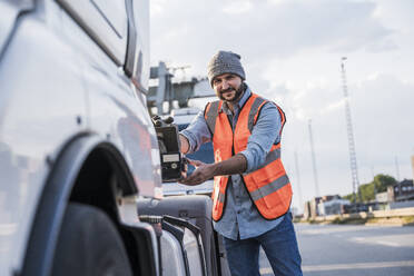 Smiling truck driver touching truck on road - UUF29568