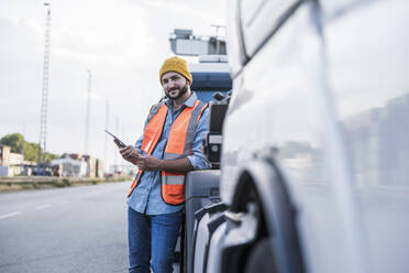 Smiling truck driver leaning on truck with tablet PC - UUF29571