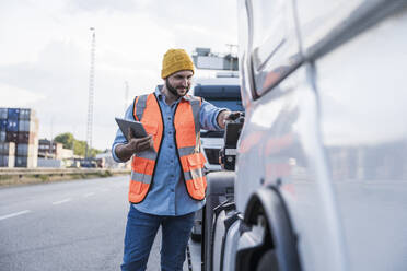 Smiling truck driver examining truck on road - UUF29572