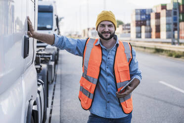 Smiling truck driver standing with tablet PC by truck - UUF29574