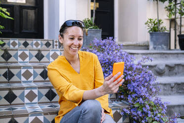 Smiling woman taking selfie through smart phone sitting on steps - AMWF01564