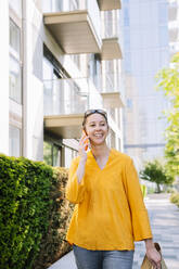 Lächelnde Frau, die mit ihrem Smartphone telefoniert und auf einem Fußweg geht - AMWF01566