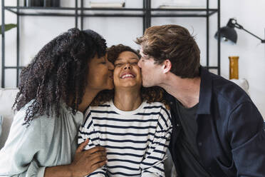 Happy daughter sitting between parents kissing her on the cheeks - PNAF05605