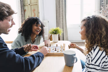 Eltern sitzen im Wohnzimmer und bringen ihrer Tochter das Schachspielen bei - PNAF05637