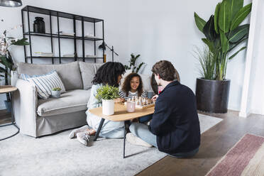 Parents sitting in livingroom teaching daughter to play chess - PNAF05638