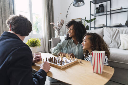 Parents sitting in livingroom teaching daughter to play chess - PNAF05639