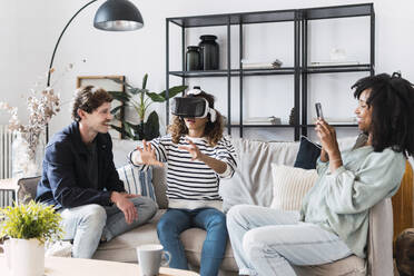 Family sitting on couch mother taking pictures of daughter using virtual reality simulator - PNAF05647