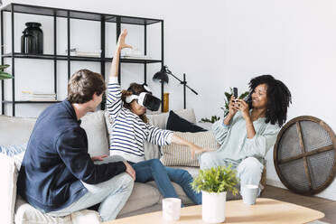 Family sitting on couch mother taking pictures of daughter using virtual reality simulator - PNAF05648