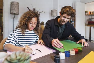 Father and daughter sitting at table drawing and painting together - PNAF05682