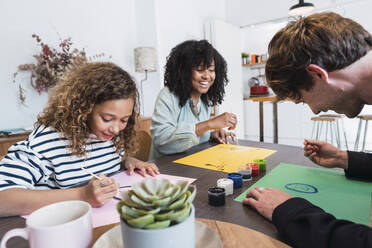 Family sitting at table drawing and painting together - PNAF05688