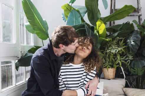 Vater küsst Tochter auf die Wange sitzend im Wintergarten - PNAF05703