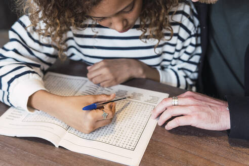 Father observing daughter solving a puzzle in a puzzle book - PNAF05713