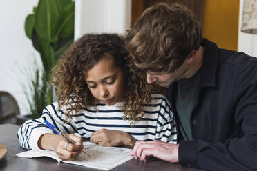 Father observing daughter solving a puzzle in a puzzle book - PNAF05714