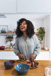 Woman standing at kitchen counter chopping healthy food - PNAF05720