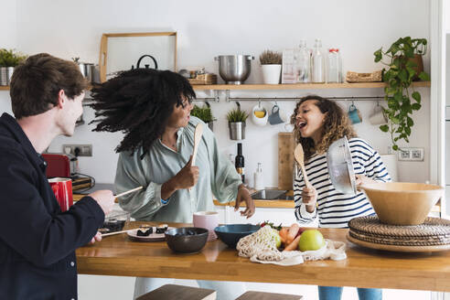 Happy family preparing food together singing and dancing in the kitchen - PNAF05735