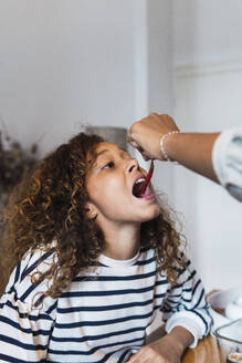 Mädchen versucht, eine scharfe Chilischote zu essen, die von der Hand der Mutter gehalten wird - PNAF05749