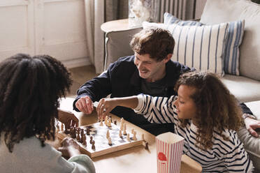 Eltern sitzen im Wohnzimmer und bringen ihrer Tochter das Schachspielen bei - PNAF05759